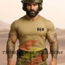 Cargar imagen en el visor de la galería, Hombre de frente con camiseta táctica fabricada en algodón, en color arena de la marca Depredador Hispano en un entorno desértico. En el pecho lleva un logotipo con con las iniciales de la marca (DH) y un fusil de asalto G36 en vertical. Ropa militar de alto rendimiento con diseño reivindicativo de poder hispano.
