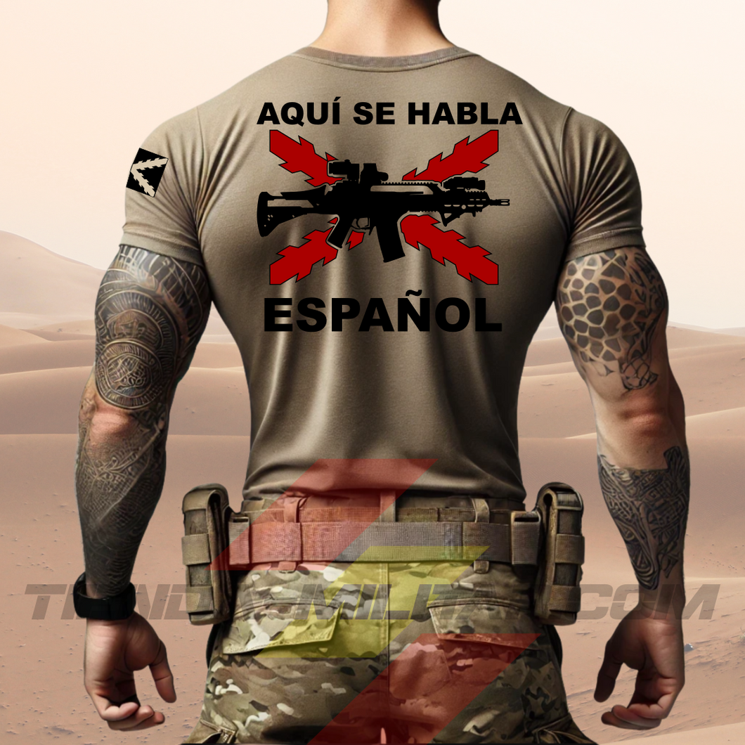 Hombre de espaldas con camiseta táctica color arena de Depredador Hispano en un entorno desértico. En el pecho lleva un logotipo con calavera táctica y casco, y en la espalda la frase “AQUÍ SE HABLA ESPAÑOL” junto a un fusil sobre fondo de Cruz de Borgoña. Ropa militar de alto rendimiento con diseño hispano.