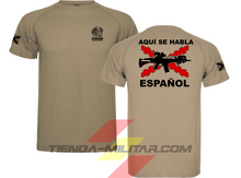 Cargar imagen en el visor de la galería, Camiseta táctica color arena de Depredador Hispano en un entorno desértico. En el pecho lleva un logotipo con calavera táctica y casco, y en la espalda la frase “AQUÍ SE HABLA ESPAÑOL” junto a un fusil sobre fondo de Cruz de Borgoña. Ropa militar de alto rendimiento con diseño hispano.
