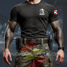 Cargar imagen en el visor de la galería, Hombre de frente con camiseta táctica color negro de Depredador Hispano en un entorno desértico. En el pecho lleva un logotipo con calavera táctica y casco, y en la espalda la frase “AQUÍ SE HABLA ESPAÑOL” junto a un fusil sobre fondo de Cruz de Borgoña. Ropa militar de alto rendimiento con diseño hispano.
