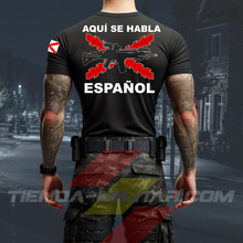 Cargar imagen en el visor de la galería, Hombre de espaldas con camiseta táctica color negro de Depredador Hispano en un entorno desértico. En el pecho lleva un logotipo con calavera táctica y casco, y en la espalda la frase “AQUÍ SE HABLA ESPAÑOL” junto a un fusil sobre fondo de Cruz de Borgoña. Ropa militar de alto rendimiento con diseño hispano.
