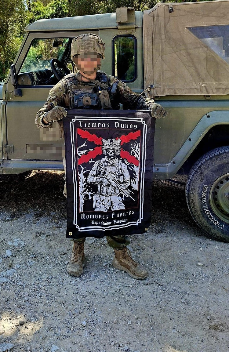 Militar con la Bandera Tiempos Duros Hombres Fuertes de Depredador Hispano junto a un vehículo militar.